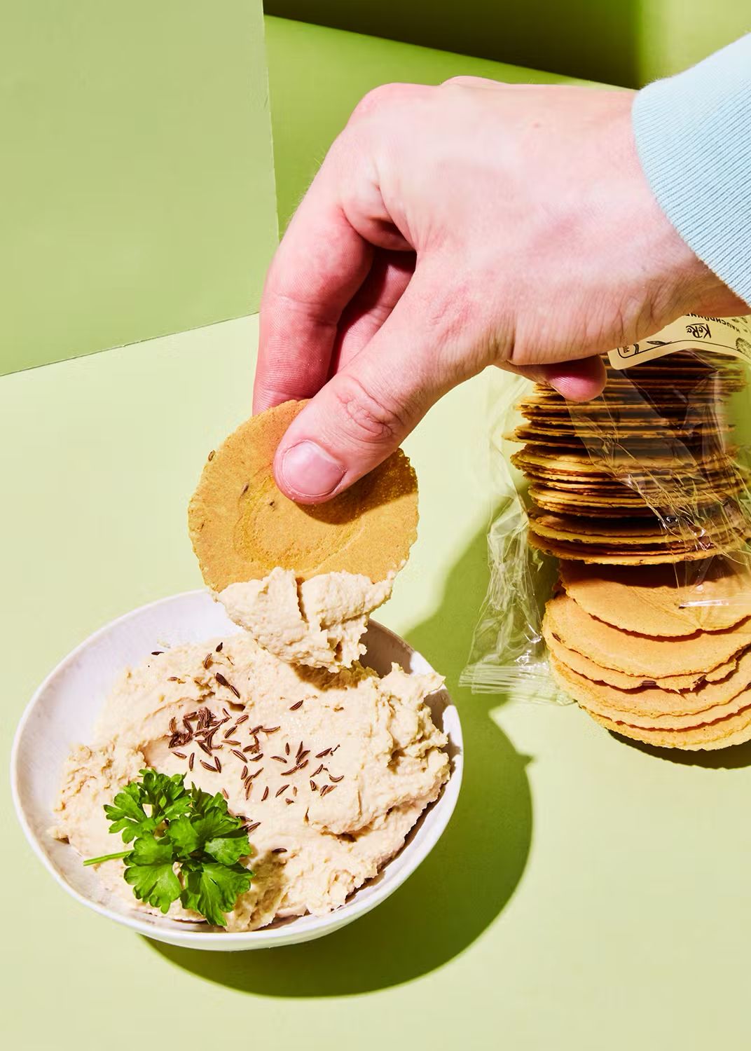 Stack of KoRo Hauchdünne Cracker next to a bowl of hummus dip